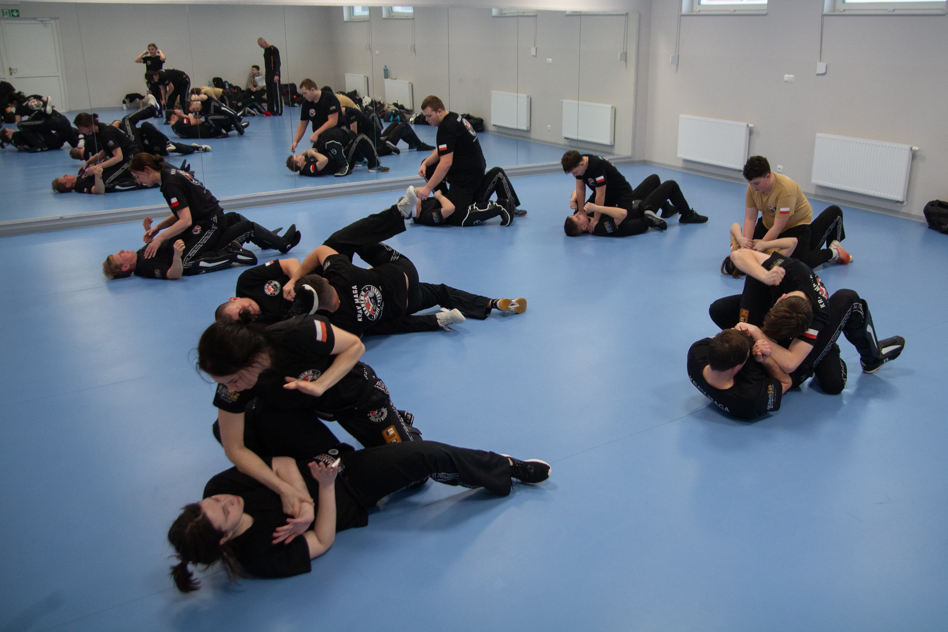 Panorama sali treningowej — pary ćwiczą ground fight w Akademii Samoobrony